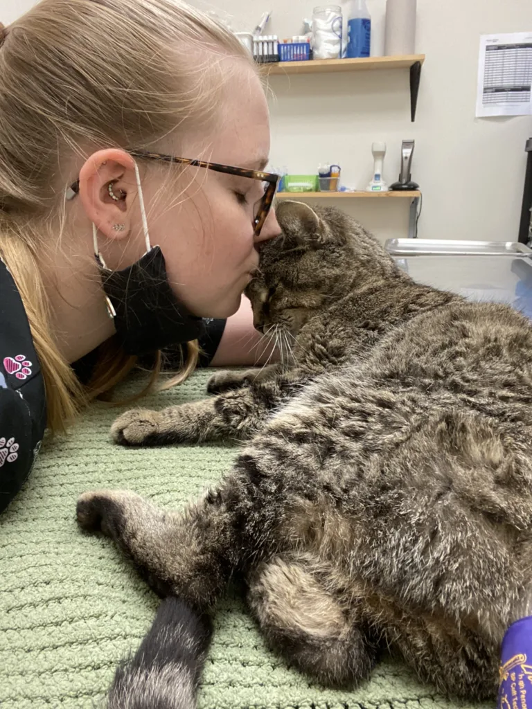 A photo of a person named Sydni Martin in a vet clinic kissing a kitty client