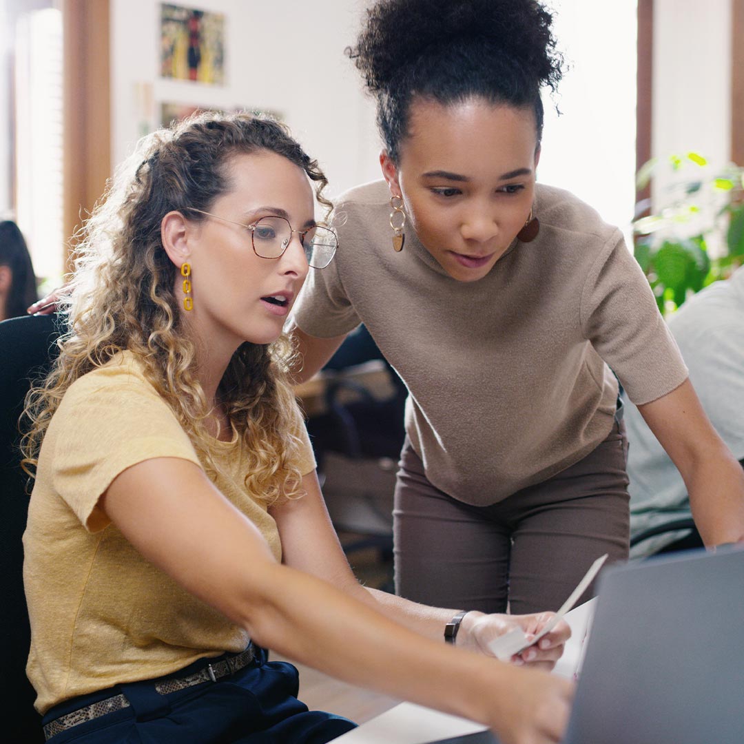 two women discussing something on laptop screen in officd